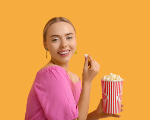 Poster - Happy young woman with bucket of popcorn on orange background