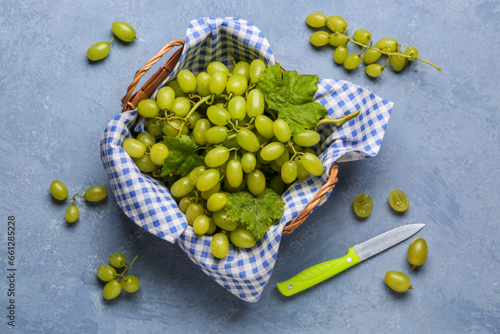 Picnic basket with ripe green grapes on color background, top view