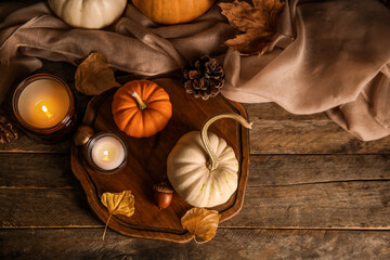 Wall Mural - Board with burning candles, pumpkins, autumn leaves, scarf and acorns on wooden background