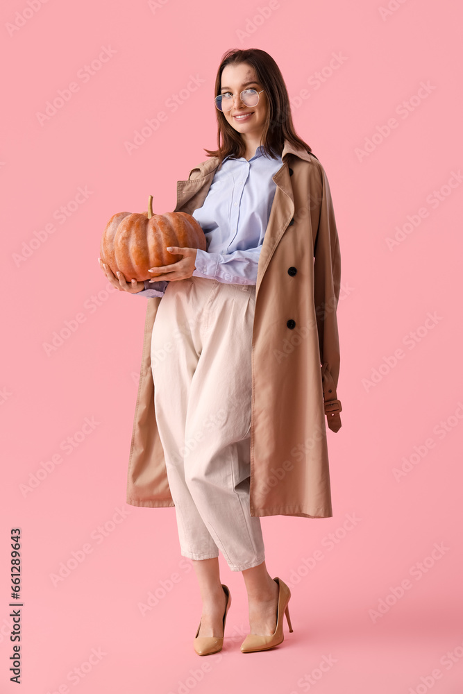 Beautiful young woman with pumpkin on pink background