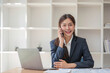 © wichayada - Attractive Asian woman using laptop in online meeting. Businesswoman using mobile phone talking with colleague sitting at table in modern office