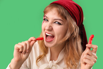 Poster - Young woman dressed for Halloween as pirate eating jelly fingers on green background, closeup