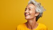 The adult woman is aging gracefully with smooth, healthy facial skin with a gray glow and a cheerful smile on yellow background. Beauty and cosmetic skin care advertising concept. 