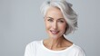 The adult woman is aging gracefully with smooth, healthy facial skin with a gray glow and a cheerful smile on gray background. Beauty and cosmetic skin care advertising concept. 