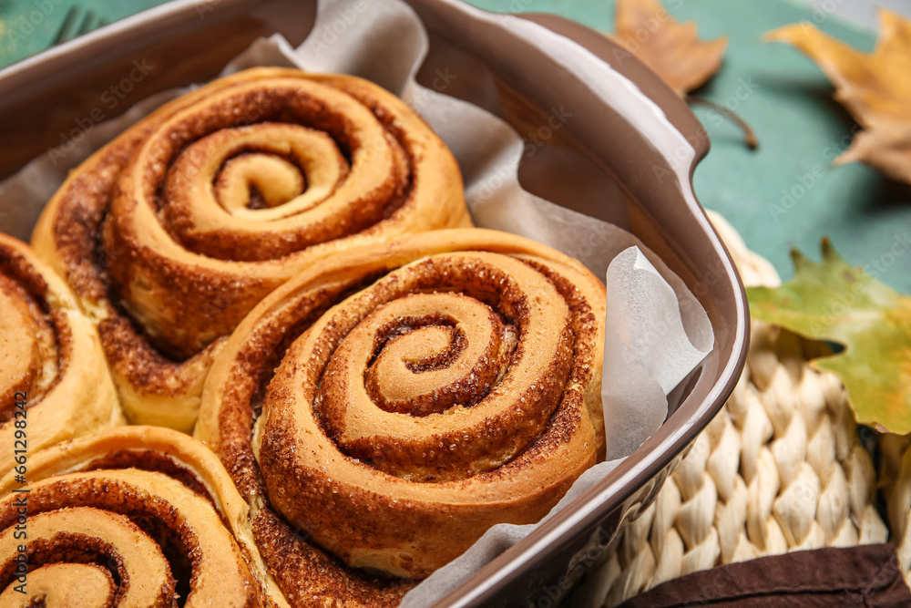 Baking dish of tasty cinnamon rolls on green background