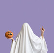 © Pixel-Shot - Woman in Halloween costume of ghost with pumpkin pointing at something on lilac background