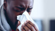 A dark-skinned young man allergy or flu sufferer blows his nose or sneezes into a handkerchief.