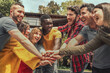 © Lomb - Multiracial Youth Group Uniting Hands Outdoors - Multiracial young individuals in a circle join hands outdoors; they celebrate with joy, looking into each other's eyes.