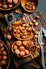 Wall Mural - Nuts background. Hazelnuts in a bowl, nut kernels and Nutcracker, tongs for nuts on a dark stone table. Vertical photo.