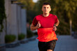 © master1305 - Focused and concentrated man in his 30 in red sportswear, running athlete in motion, running outdoors on empty street. Concept of sport, active and healthy lifestyle, competition, dynamics, marathon