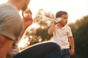 Wall Mural - Fun, holding and using string can phone. Father and little son are playing outdoors