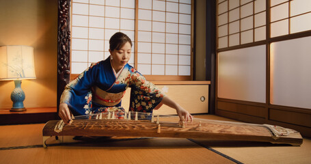 Portrait of a Talented Female Playing Koto Plucked String Instrument in Traditional Japanese Home. Musician Wearing a Blue Kimono, Practicing to Play Historic Music Before a Concert