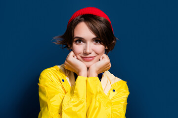 Poster - Closeup photo of young girl brown hair touch cheeks posing wear yellow coat dreamy cute outdoors tourist isolated on blue color background