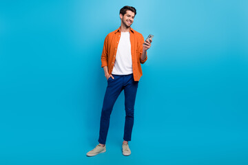 Fototapete - Full body photo of cheerful young man hold use smart phone chatting blogging isolated on blue color background