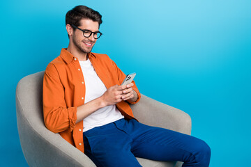 Fototapete - Portrait of handsome cheerful person sitting cozy soft chair use smart phone chatting communicate isolated on blue color background