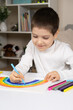 © Zarina Lukash - A small child draws a rainbow with felt-tip pens in a sketchbook while sitting at a table