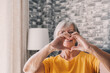 © Daniel - Elderly woman sit in living room connected fingers showing heart symbol close up, old people cardiovascular disease prevention treatment, health check-up, cardio vitamins, sign of kindness and charity