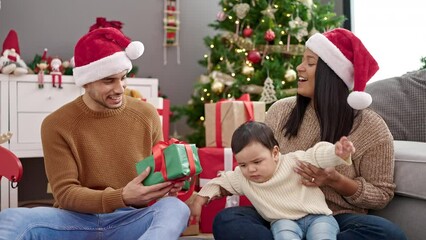 Poster - Couple and son holding gift sitting on floor by christmas tree at home