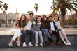 © CarlosBarquero - Portrait of joyful group of happy young multi-ethnic friends enjoying vacation in European city. Multiracial people sitting in line in square looking at camera for souvenir photo of trip abroad.