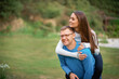 © Olga - Loving spouses family boyfriend and girlfriend wife and husband hugging embracing on date in a park. Handsome young man giving his girlfriend a piggyback ride at park while looking in camera.