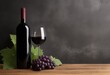A concrete wall background with a bunch of grapes on a wooden table and an antique red wine bottle with an unlabeled matte black label. Copy space for text ,advertising, message, logo