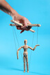 © New Africa - Man pulling strings of puppet on light blue background, closeup