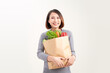 Young asian girl holding paper bag with vegetable looking positive and happy on white background