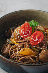 Wall Mural - noodles with beef, vegetables, cherry tomatoes and sesame sauce in a deep plate side view