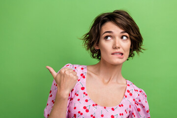 Sticker - Photo of attractive young woman point frightened empty space dressed stylish pink cherry print clothes isolated on green color background