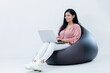 © Photographielove - Indian female with laptop sitting on Bean bag on isolated white background and smiling
