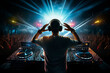 Back view of a DJ greeting an enthusiastic crowd at huge party dance music event, surrounded by vivid neon lights.