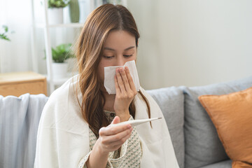 Wall Mural - Sick, influenza asian young woman tired have a fever and sore cough hand holding thermometer for check measure body temperature, illness while rest at home. Health care with disease, pandemic virus.