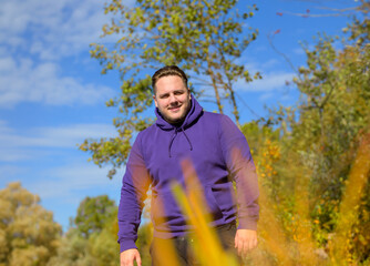 Wall Mural - Young attractive man wearing a purple hoodie behind some bushes
