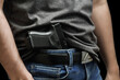 Hided handgun under the denim belt. a man in jeans and a t-shirt holds a gun in his hand from the back