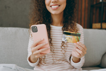 Wall Mural - Cropped yyoung happy woman in casual clothes sits on grey sofa couch using mobile cell phone credit bank card shopping online stay at home hotel flat rest relax spend free time in living room indoor