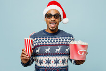 Young Excited Man In 3d Glasses Wear Knitted Sweater Santa Hat Posing Watch Movie Film Hold Bucket Of Popcorn Cup Of Soda Pop In Cinema Isolated On Plain Pastel Blue Background. Happy New Year 2024.