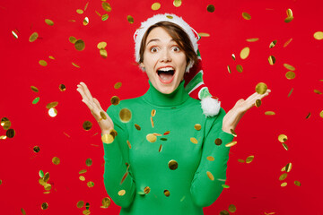 Wall Mural - Young woman wear warm green turtleneck Santa hat posing spread hands look camera in falling confetti around isolated on plain red background. Happy New Year 2024 celebration Christmas holiday concept.