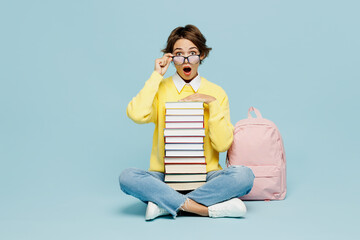 Wall Mural - Full body young shocked amazed woman student wear casual clothes sweater backpack bag lower glasses hold stack of many books isolated on plain blue background. High school university college concept.