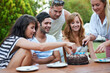 © Marine G/peopleimages.com - Birthday, friends and cutting cake outdoor for celebration, surprise or party with milestone or happiness. Dessert, men and women in backyard of home with gathering or social event with smile and fun
