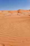 Fototapeta Miasto - Wavy orange sand imprint against a backdrop of sand dunes and blue sky.