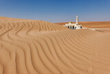 Fototapeta Miasto - In the background is a white mosque semi-covered by a Wahiba desert dune in the foreground waves of sand.
