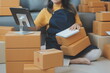 © Sirikarn Rinruesee - Startup SME small business entrepreneur of freelance Asian woman using a laptop with box Cheerful success Asian woman her hand lifts up online marketing packaging box and delivery SME idea concept