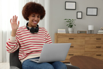 Wall Mural - Beautiful young woman having video chat via laptop and saying hello in room, space for text