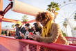 © CarlosBarquero - Smiling young persons using cell phones. Teenagers addicted to online technological trends. Group of friends leaning on a railing checking their social networks. People gathered at the amusement park.