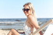 © rogerphoto - Happy blonde woman wearing sun glasses and relaxing on a wooden deck chair at the ocean beach