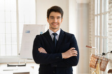 Happy Handsome Young Business Leader, Entrepreneur Man Working In Millennial Office Boardroom, Standing With Arms Folded, Looking At Camera, Smiling, Enjoying Confidence. Professional Portrait