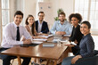 © fizkes - Happy young diverse team of professionals posing at office table, looking at camera, smiling, meeting for discussion creative ideas, brainstorming on startup project strategy. Corporate portrait