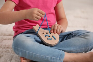 Sticker - Little girl playing with wooden lacing toy on carpet indoors, closeup