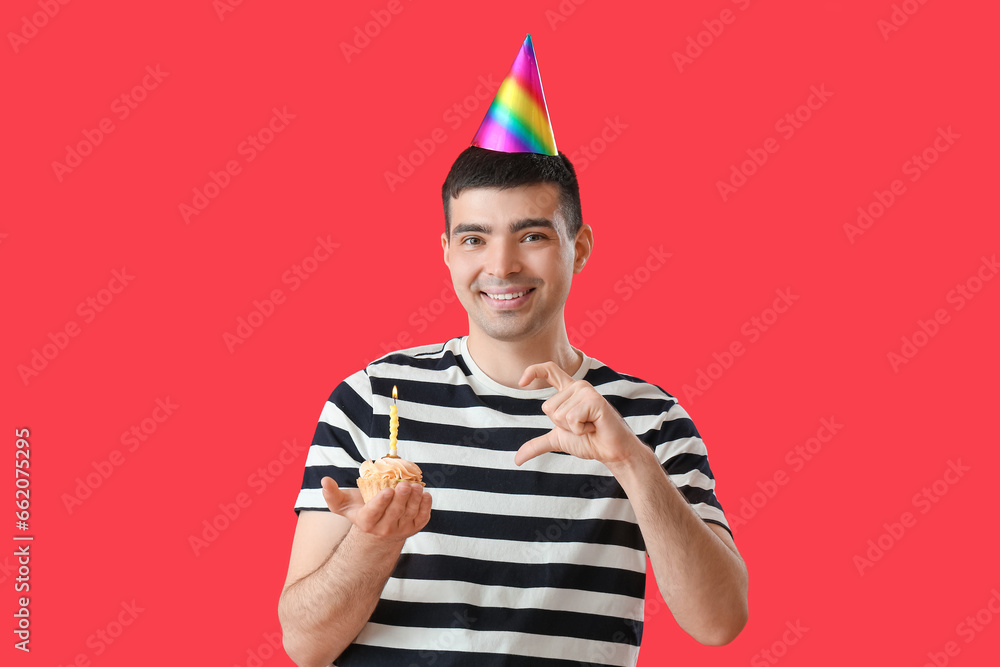 Young man with birthday cake making heart with his hand on red background