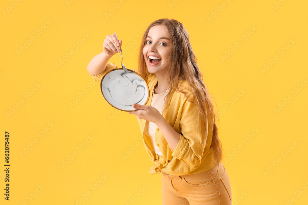 Beautiful young woman with empty plate and spoon on yellow background